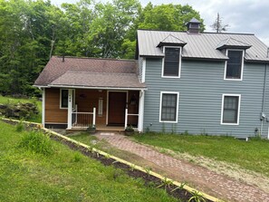 Ein zweistöckiges Haus mit Veranda, Schornstein und einem Weg zum Eingang.