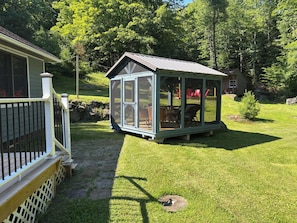 A glass-enclosed outdoor seating area with a wooden deck and a stone pathway leading to it. - Private Modern Adirondack Home (Saranac Lake)