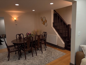 A dining area with a round table, chairs, a vase of flowers, a wall-mounted light fixture, and a staircase. - Private Modern Adirondack Home (Saranac Lake)