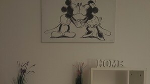 Ett rum med ett vitt skrivbord, en vit hylla och en tavla på väggen som föreställer två tecknade figurer.