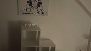Ett rum med en vit vägg, en inramad bild på två tecknade figurer och en vit förvaringsenhet med ordet ”HEM” skrivet ovanpå.