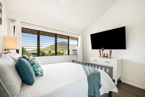 A bedroom with a bed, a window with a view, a flat-screen TV, and a dresser. - Just Listed! Banyan Retreat at Kalapaki Bay Beach (Lihue)