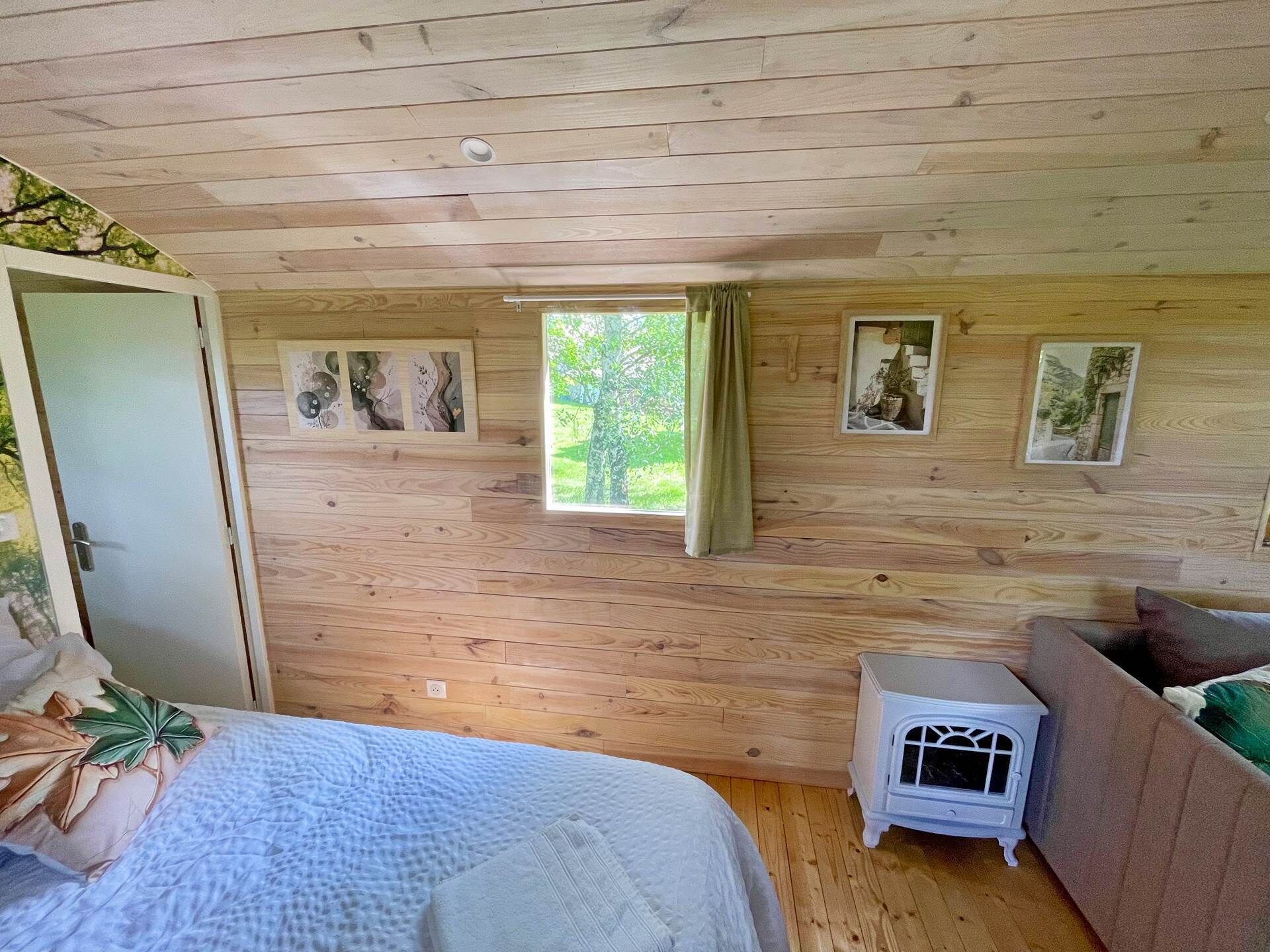 A wooden-paneled room with a bed, a small white heater, and framed pictures on the wall.