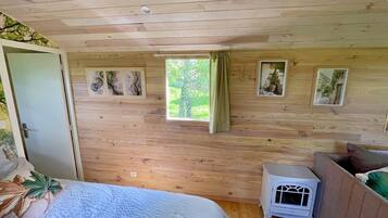 A wooden-paneled room with a bed, a small white heater, and framed pictures on the wall.