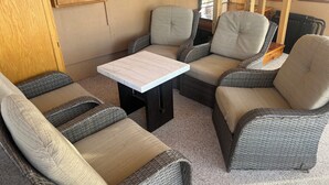 Um espaço de estar aconchegante com móveis de vime e uma mesa de mármore, com um armário de madeira e uma escada ao fundo.
