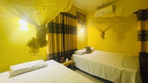 A room with two beds, a mosquito net, and a wall-mounted air conditioner. - Nilmini Lodge (Sigiriya)