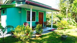 A small, single-story house with a green exterior and a porch. There are potted plants and a small table outside. - Nilmini Lodge (Sigiriya)