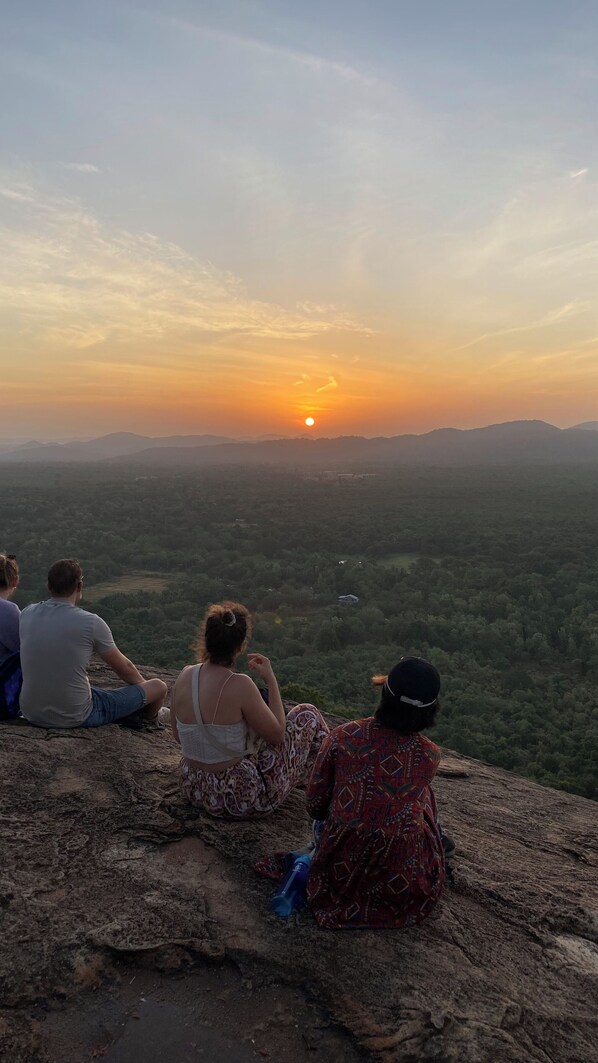 A group of people sitting on a rocky outcrop overlooking a valley during sunset. - Nilmini Lodge (Sigiriya)