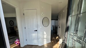Um corredor com piso de madeira, porta branca, espelho e porta de vidro que dá para outro quarto.