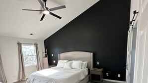 Quarto moderno com uma cama grande, ventilador de teto e parede de destaque escura.