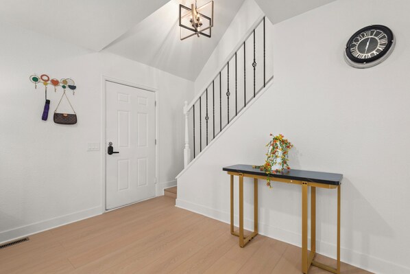 A staircase with a black and white clock, a white door, and a small table with a vase of flowers. - Ultimate Family Retreat: Backyard, Games & Comfort (Arvada)