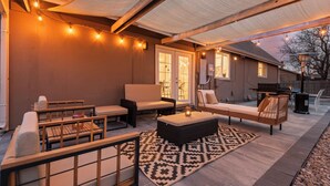 Un espace extérieur aménagé en patio, avec des sièges, un tapis à motifs et des guirlandes lumineuses.
