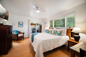 Une chambre à coucher comprenant un lit, une table de chevet, une lampe, une commode, une chaise et un ventilateur de plafond.