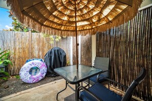 Un espace patio aménagé avec une table et des chaises, un barbecue et un grand parasol.