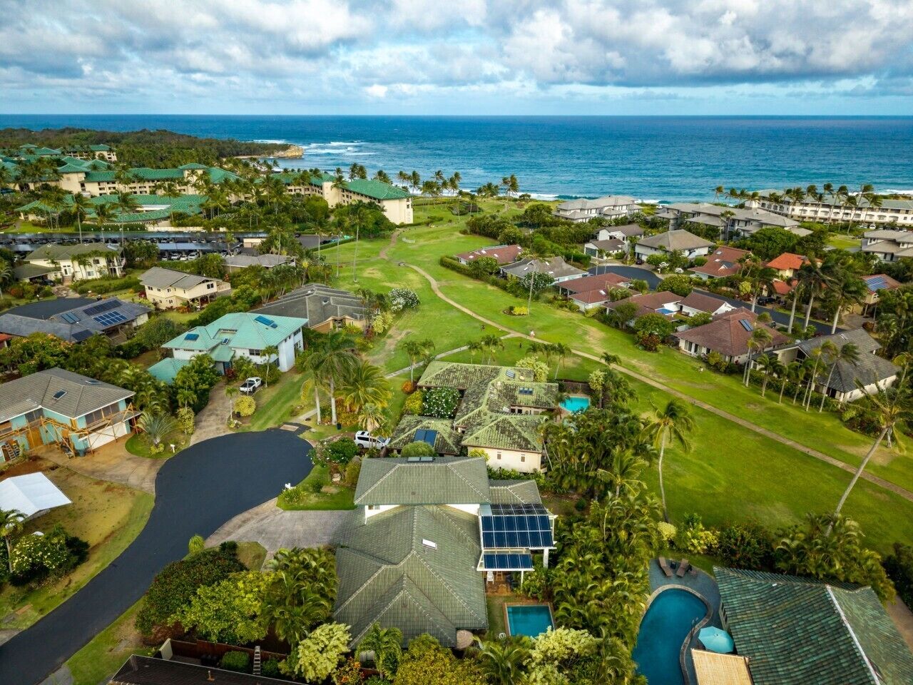 An aerial view of a coastal residential area with houses, a golf course, and a large body of water.