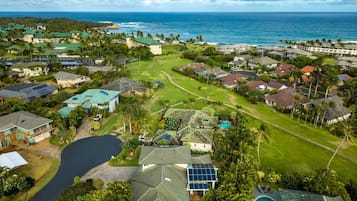 An aerial view of a coastal residential area with houses, a golf course, and a large body of water.