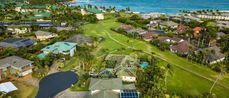 An aerial view of a coastal residential area with houses, a golf course, and a large body of water.