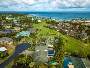Vue aérienne d’une zone résidentielle côtière, avec des maisons, un terrain de golf et une vaste étendue d’eau.
