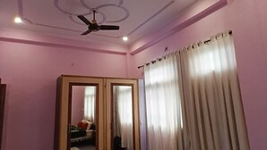 Une pièce aux murs roses, avec un ventilateur de plafond, un grand miroir et une fenêtre avec des rideaux.