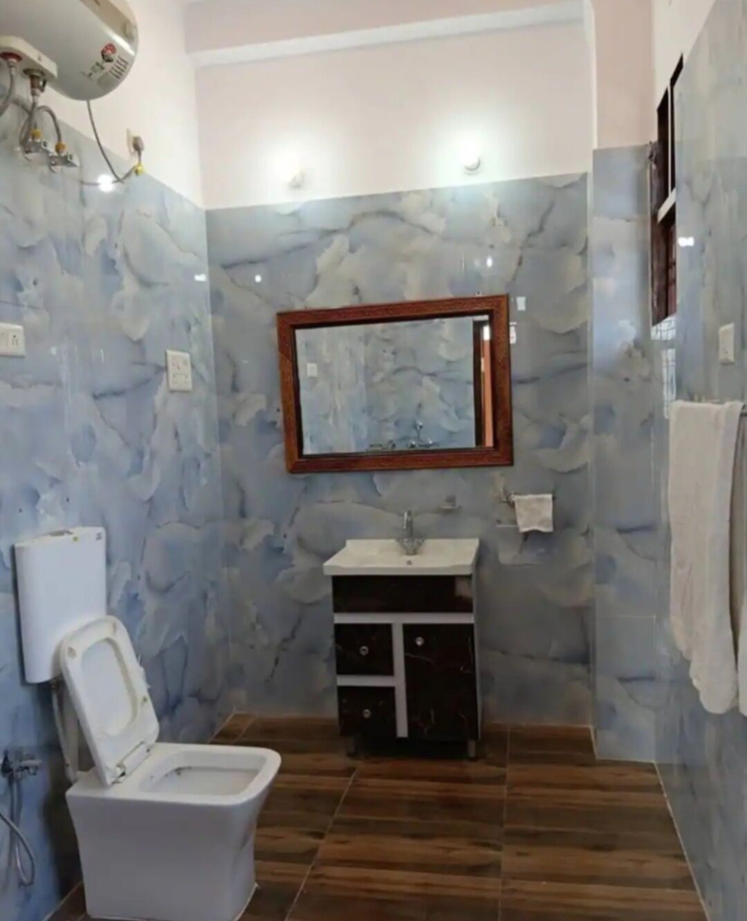 A bathroom with a marble wall, a toilet, a sink, and a mirror.