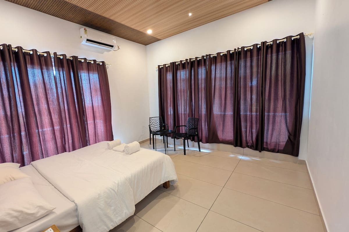 A hotel room with a bed, two chairs, a small table, and a window with curtains.