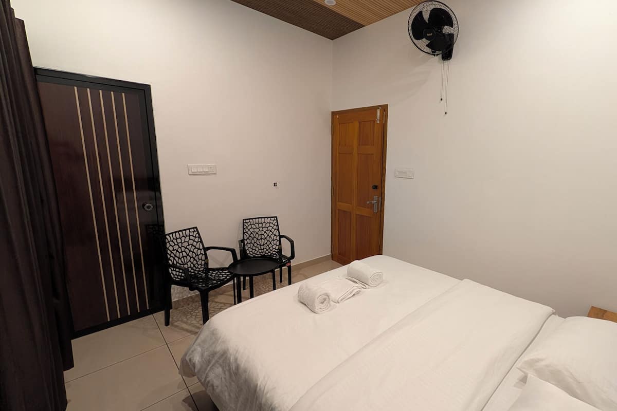 A bedroom with a bed, a wooden door, a fan, and two chairs.