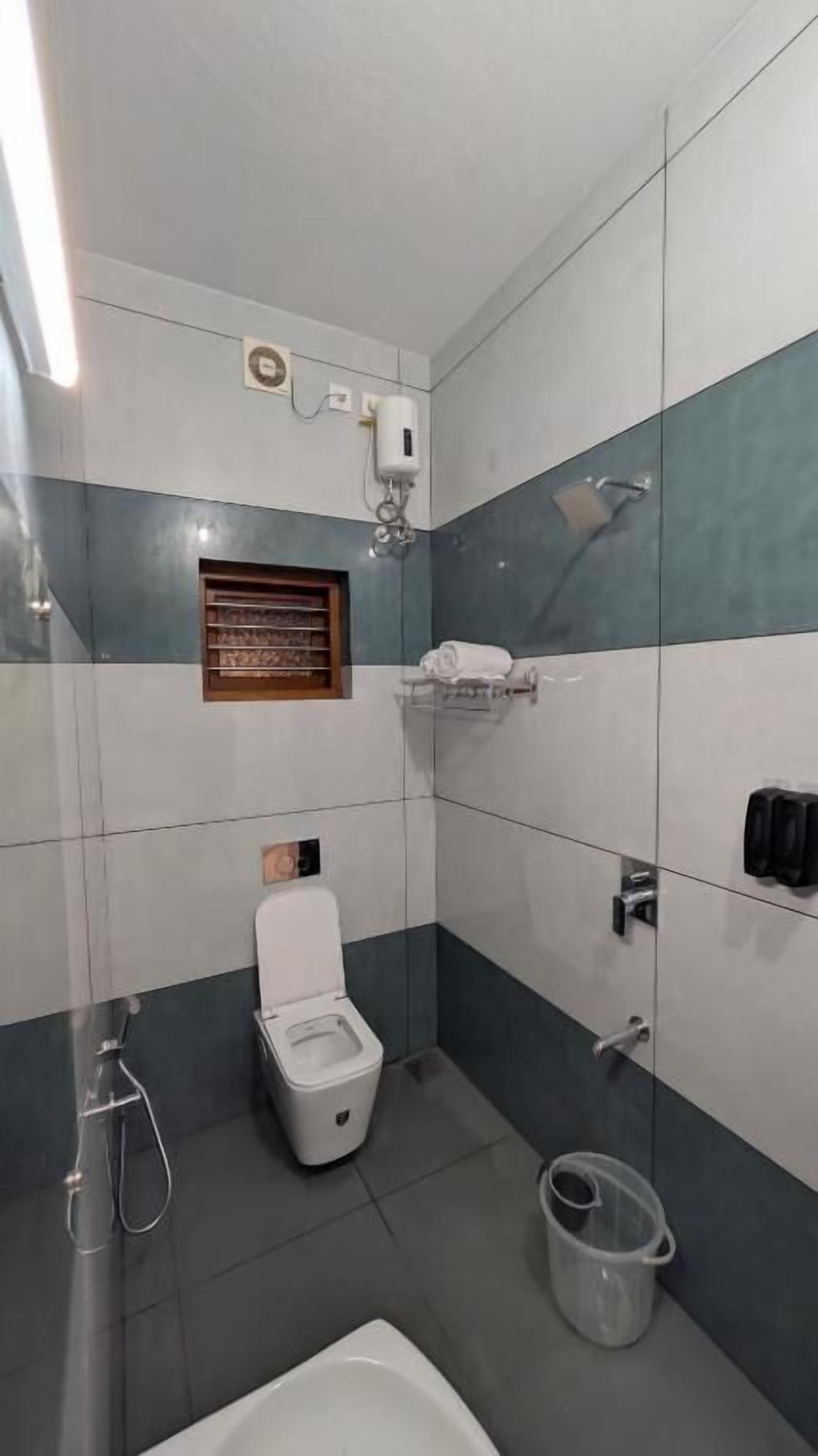 A small bathroom with a toilet, a shower, a towel rack, and a hand dryer.