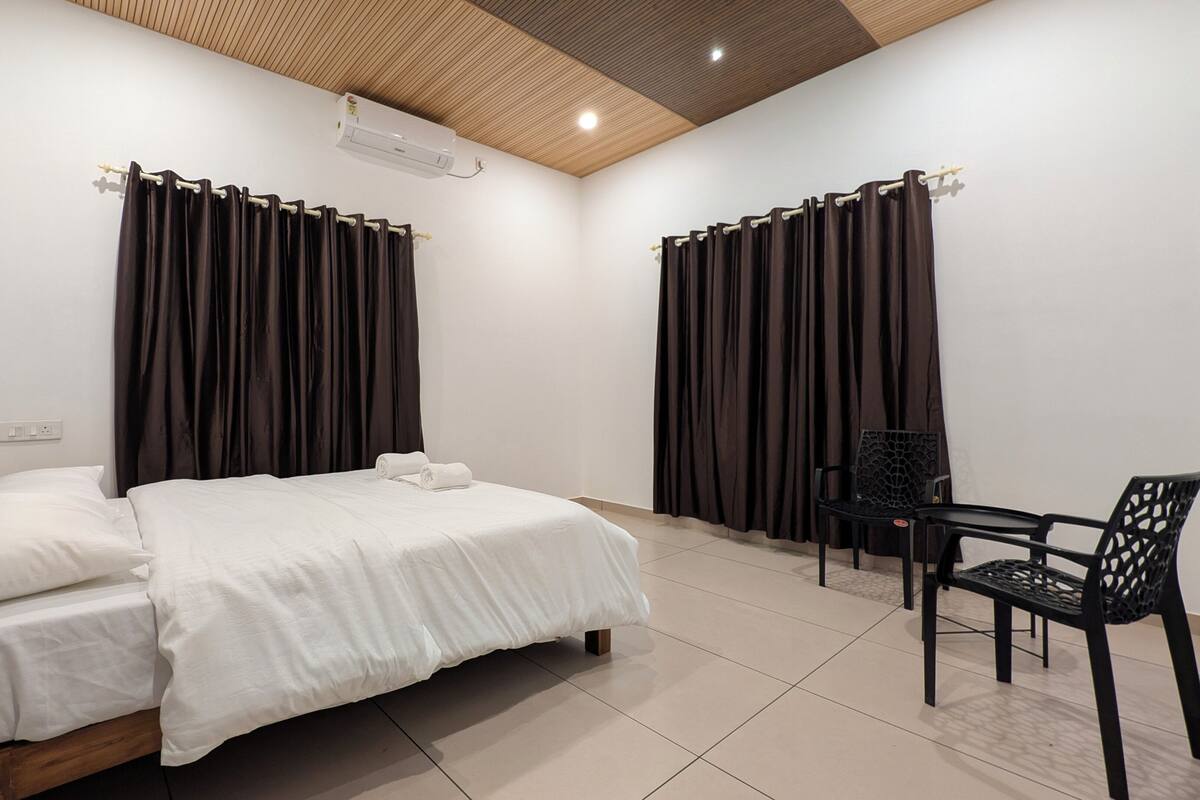 A bedroom with a bed, two chairs, a wooden headboard, and a ceiling with a wooden panel design.