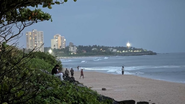 Une plage avec des gens, une côte rocheuse et des bâtiments en arrière-plan.