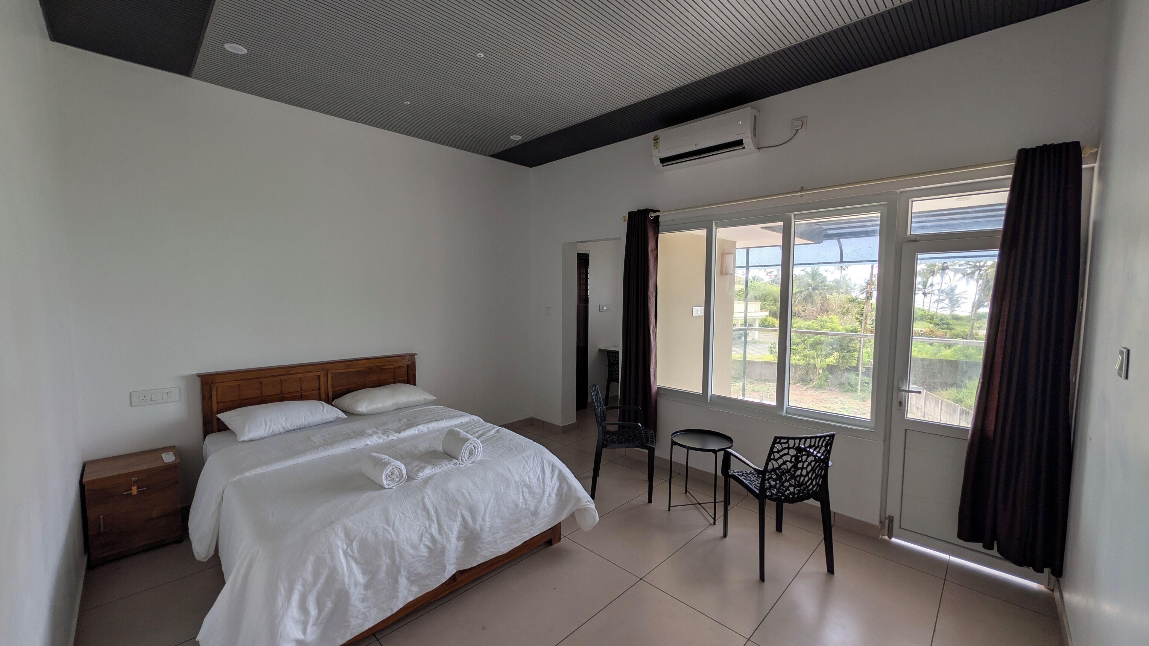 A bedroom with a bed, a wooden nightstand, a chair, and a window with curtains.