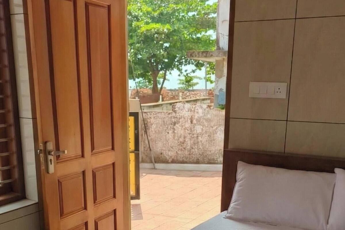A hotel room with a bed, a wooden door, and a view of the outside.