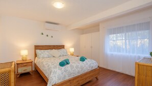 Ein Schlafzimmer mit einem Holzbett, zwei Nachttischen, einem Fenster mit durchsichtigen Vorhängen und einer Deckenleuchte.