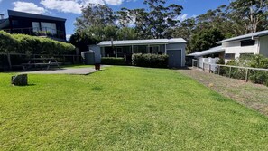 A residential property with a well-maintained lawn, a small house with a garage, and a modern building in the background. - Hop Hop House is pet friendly near the beach (Bendalong)