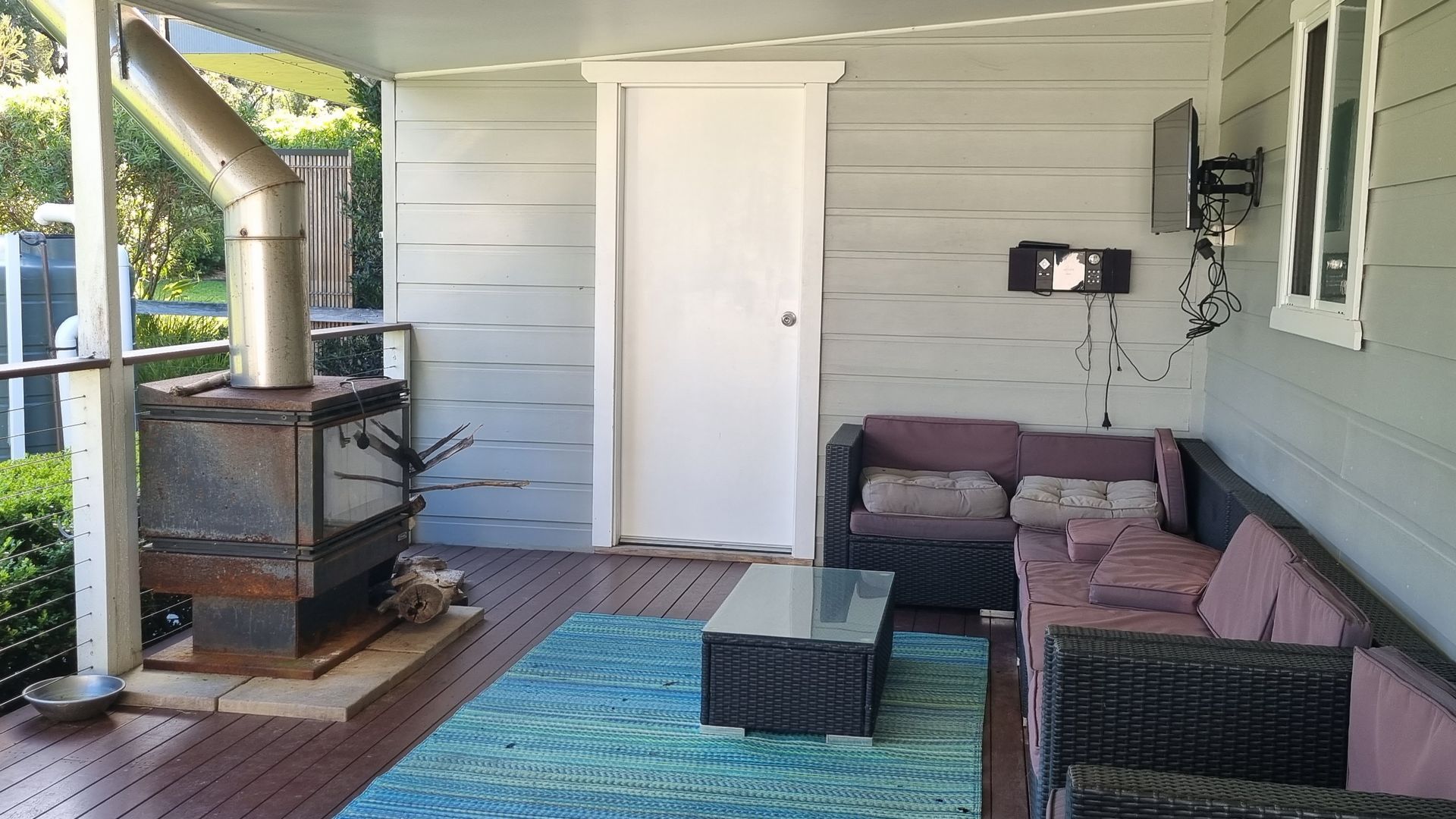 A covered porch with a wood-burning stove, a cushioned seating area, and a power outlet on the wall.
