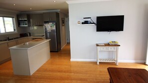 Eine moderne Küche mit einer zentralen Kochinsel, einem Essbereich mit Holztisch und einem wandmontierten Flachbildfernseher.