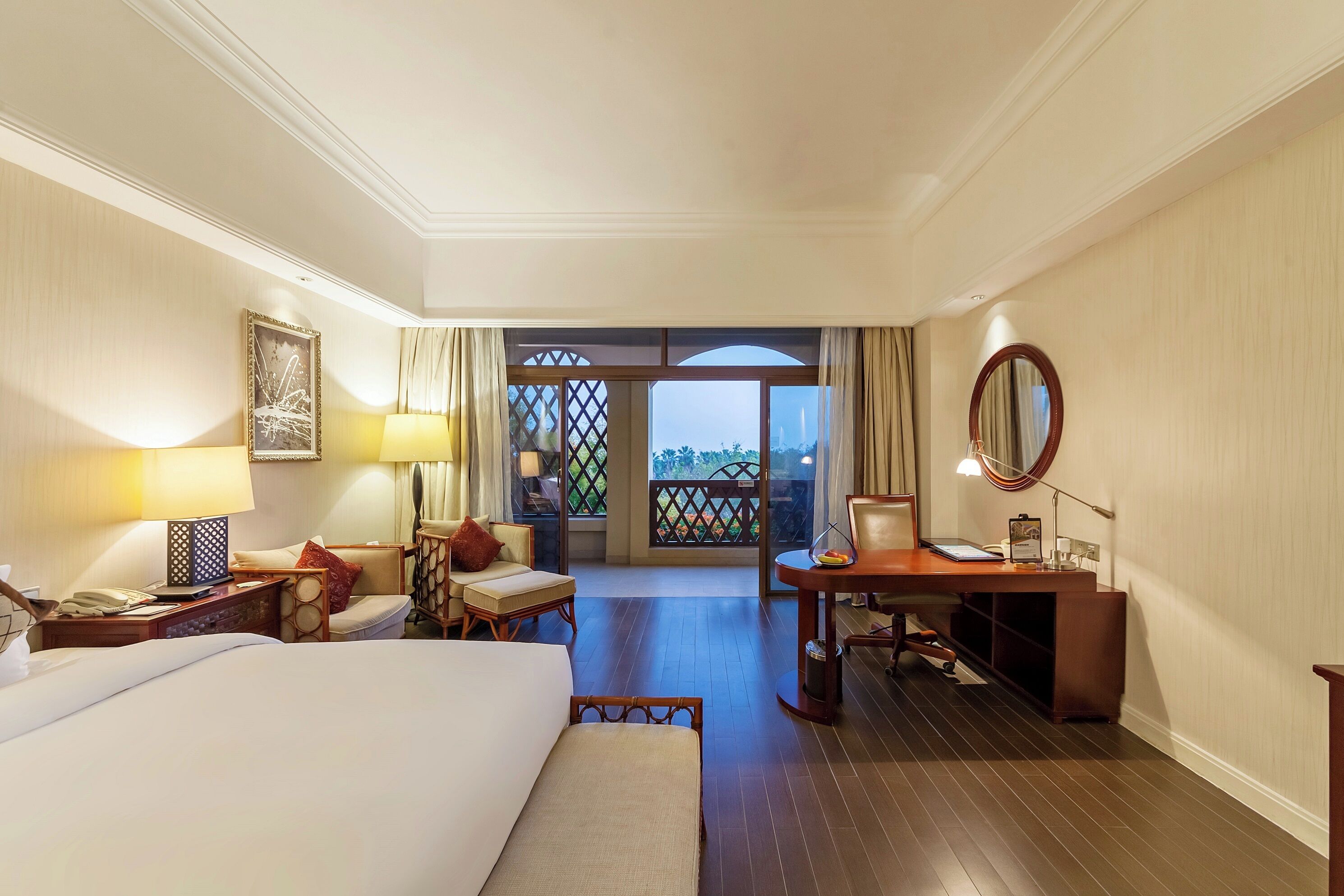 A hotel room with a bed, desk, chair, and a view of a balcony.