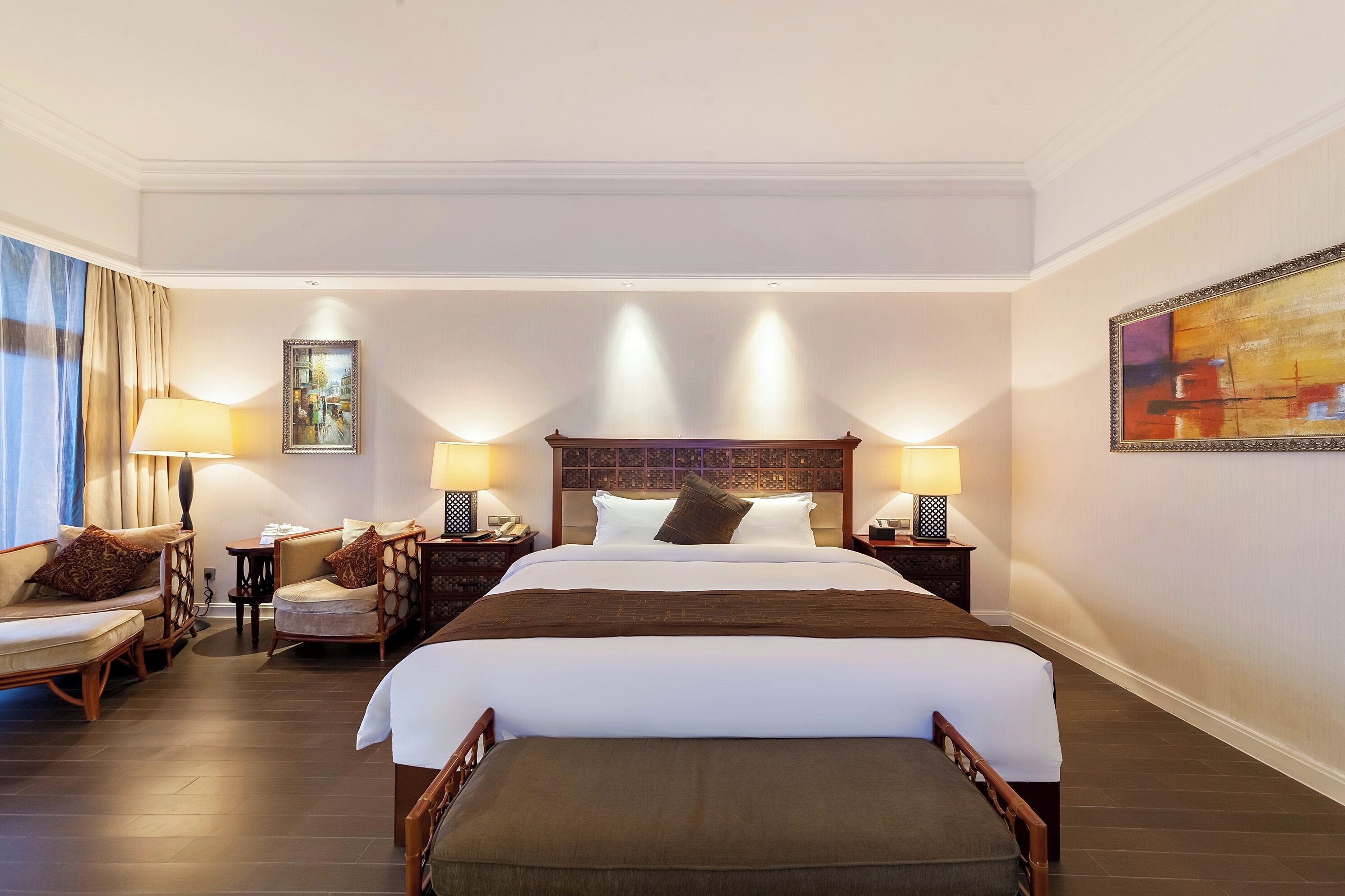 A hotel room with a large bed, two bedside tables, a chair, a sofa, and a painting on the wall.