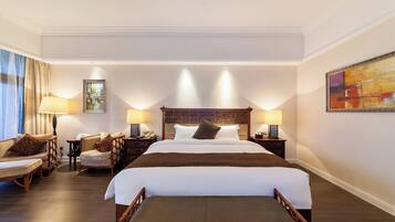 Habitación de hotel con una cama grande, dos mesitas de noche, una silla, un sofá y un cuadro en la pared.