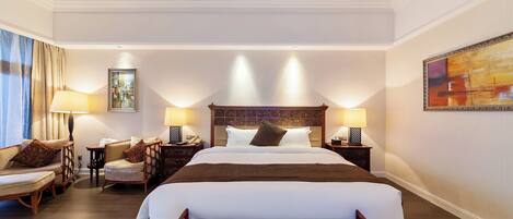 A hotel room with a large bed, two bedside tables, a chair, a sofa, and a painting on the wall.