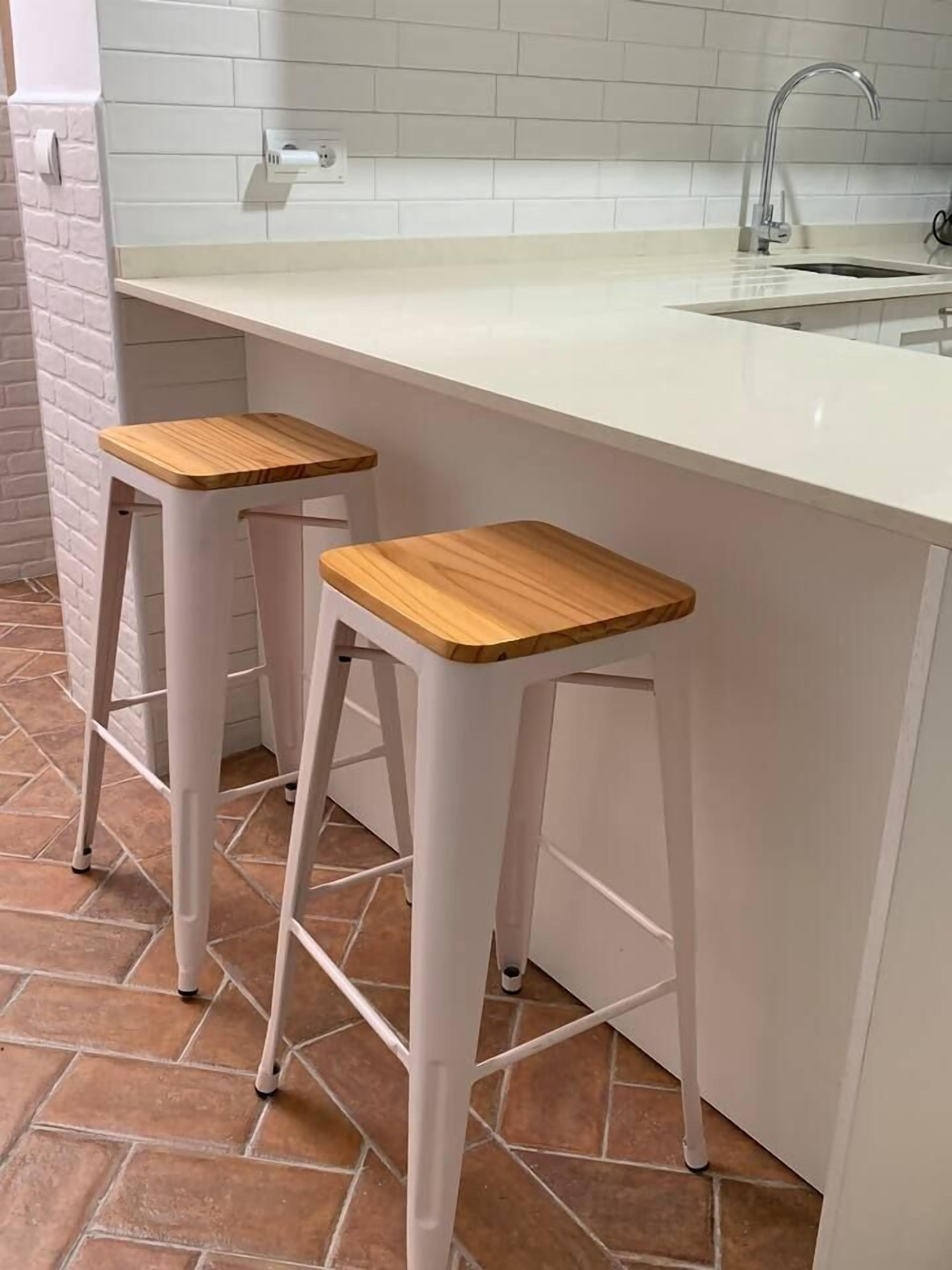 A kitchen with a white countertop, two wooden stools, and a tiled backsplash.