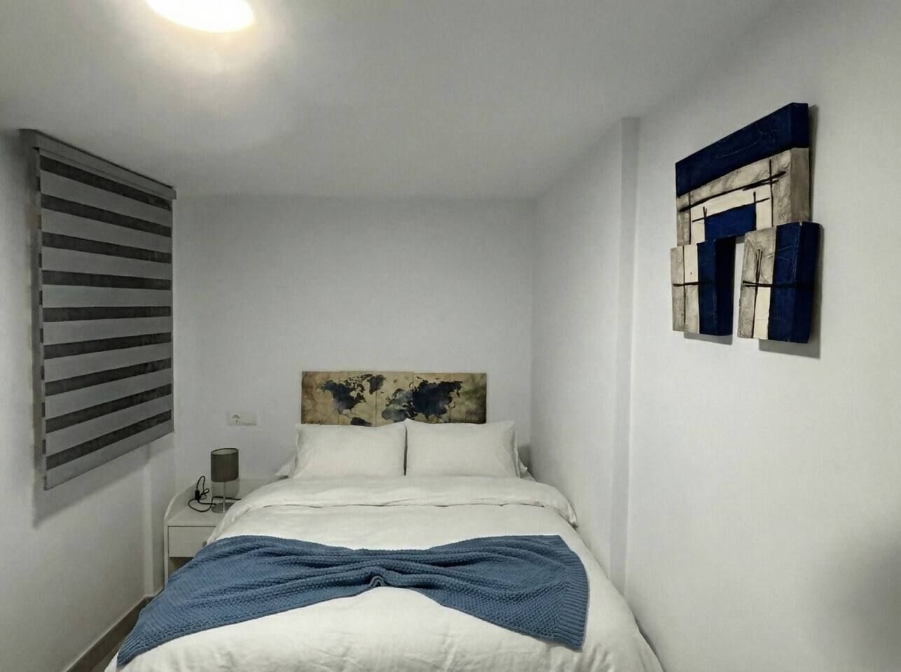 A bedroom with a bed, a nightstand, a lamp, and a wall-mounted artwork.
