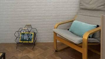 A room with a white brick wall, a framed painting, a wooden chair with a cushion, and a metal stand with a framed picture.