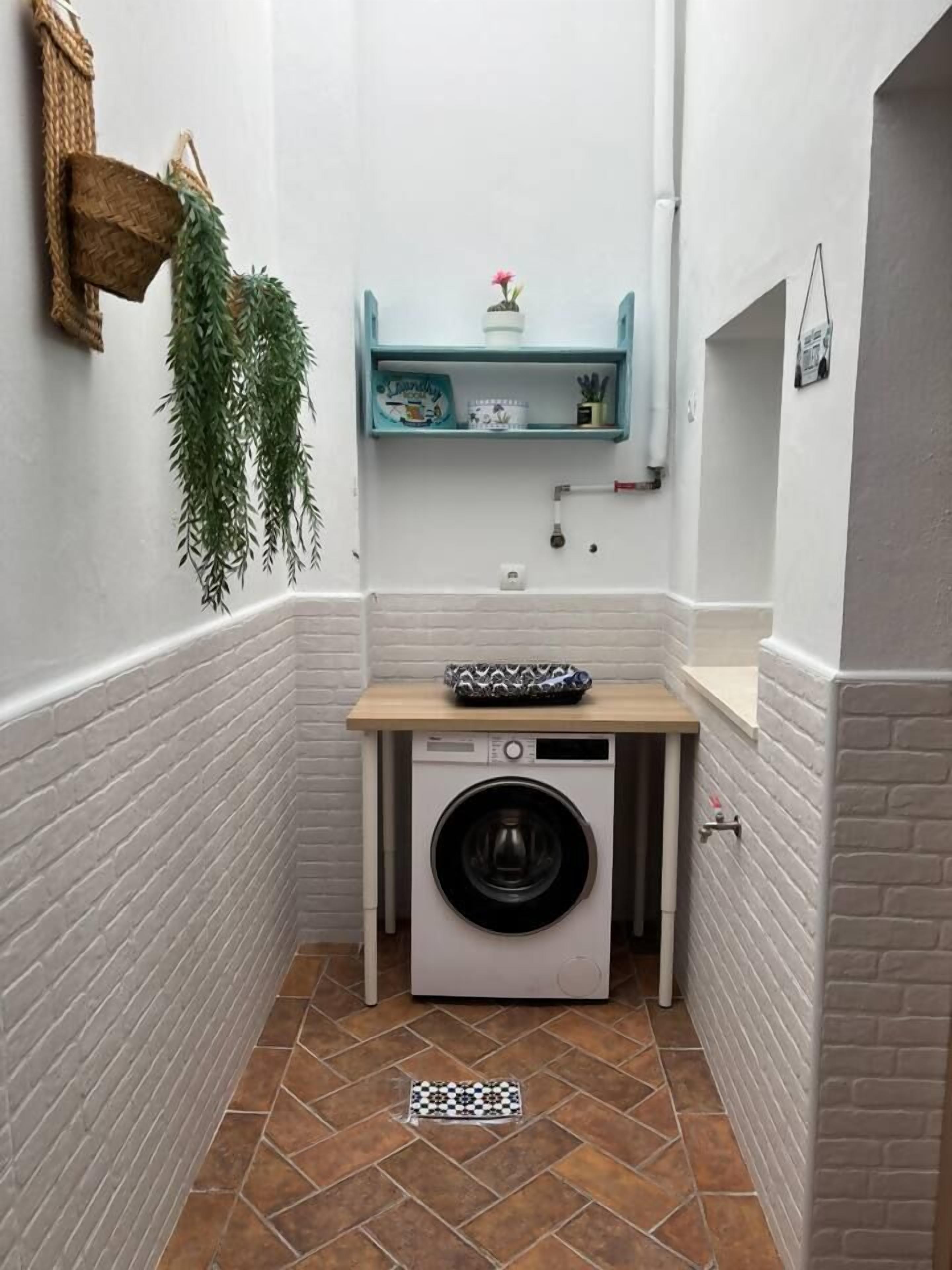 A compact laundry area with a washing machine, a shelf with toiletries, and a hanging plant.