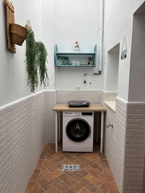 A compact laundry area with a washing machine, a shelf with toiletries, and a hanging plant. - Ecija Confort by Casa Yaye (Écija)