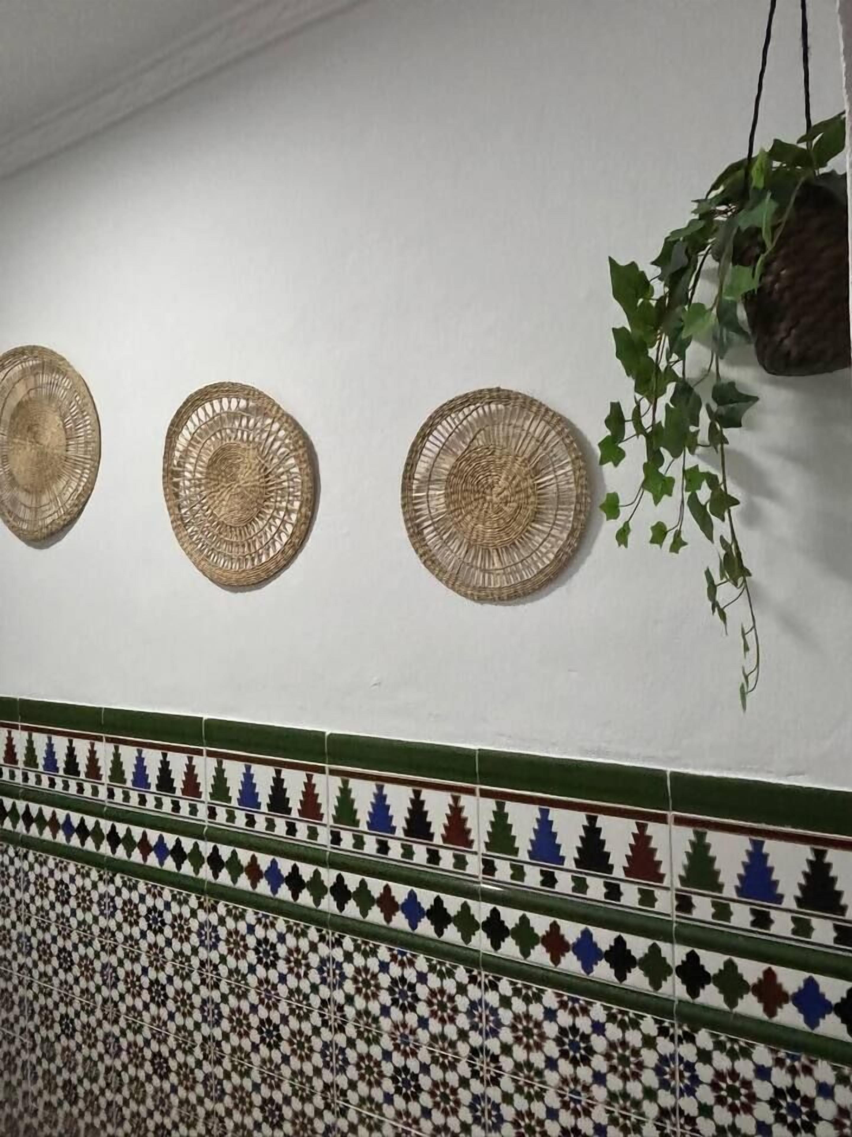 A wall with three woven wall hangings and a patterned tile border.