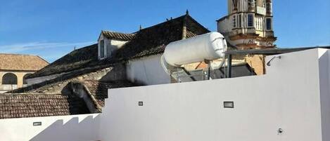 Une terrasse sur le toit, dotée d’une structure vitrée, d’un mur blanc et offrant une vue sur un bâtiment historique avec un clocher.