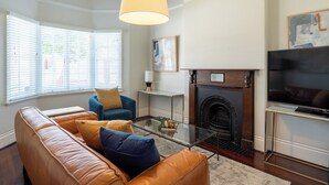 Una sala de estar con un sofá de cuero, un sillón azul, una mesa de centro de vidrio, una chimenea y un televisor.