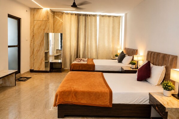 Ein Hotelzimmer mit einem großen Bett, einem kleineren Bett, einem Schreibtisch, einem Stuhl, einem Fernseher und einem Fenster mit Vorhängen.
