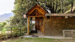 A wooden structure with a sloped roof, a brick wall, and a green metal railing. - The Silent Valley (Bhimtal)