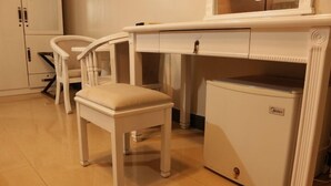 Ein kleiner Raum mit einem weißen Schreibtisch, einem Stuhl und einem kompakten Kühlschrank.